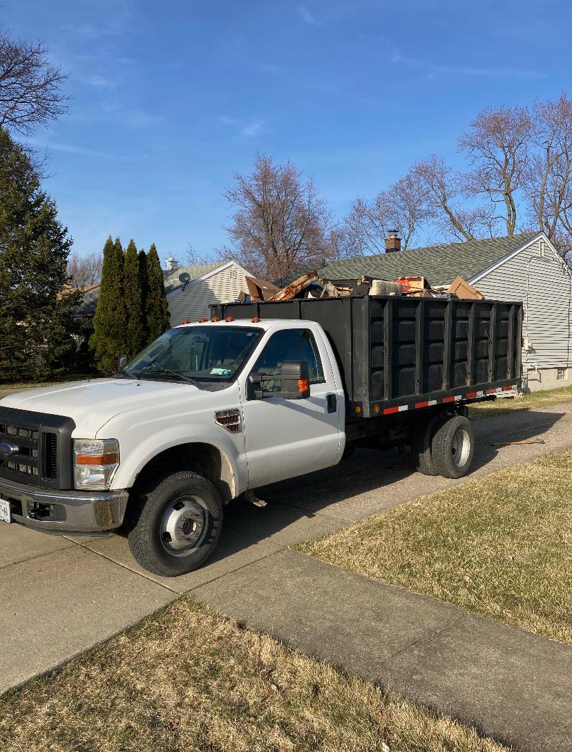 White Ford F-Series Super Duty dump truck with a black bed full of debris, parked on a suburban street.